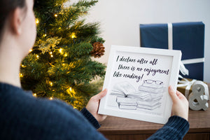 Woman holding a framed Jane Austen reading quote which reads: I declare after all their is no enjoyment like reading, displayed as a book themed christmas gift for book lovers in front of a christmas tree and christmas gifts by Wit and Widom UK