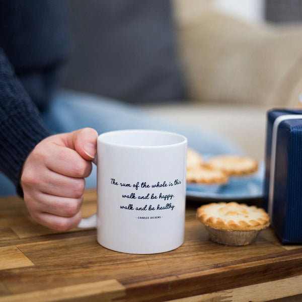 Womans hand holding a Charles Dickens walking quote on a mug on a coffee table.
