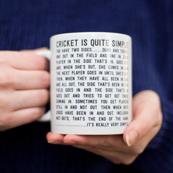 closeup of womans hands holding a white mug with womens cricket rules printed on it