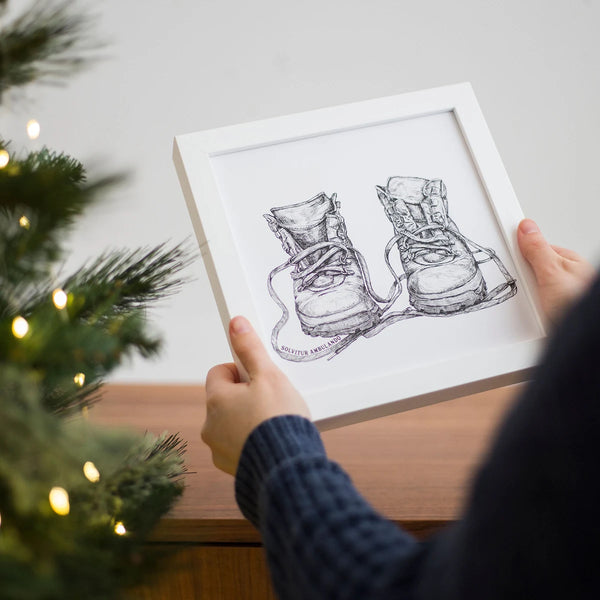 Woman holding a Motivational art featuring old leather walking boots: Solvitur Ambulando Art Print framed or unframed