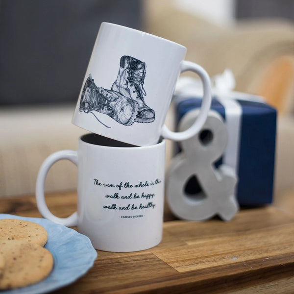 Two be happy walking quote mugs stacked with a vintage boots illustration on one mug and a walking quote on the other.