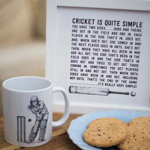 closeup of a framed cricket art print with a womens cricketer mug on a coffee table with a plate of biscuits