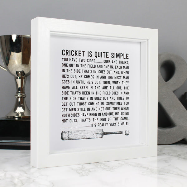 Product photo showing a black and white art print with cricket bat and ball illustration and funny cricket quote about Cricket being 'quite simple' by Wit & Wisdom. The print is displayed in a white square box frame against a grey backdrop with a trophy and grey ampersand in the background.